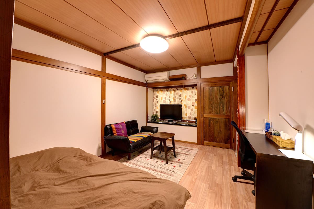 Una habitación con cama, escritorio, silla, sofá y televisor.