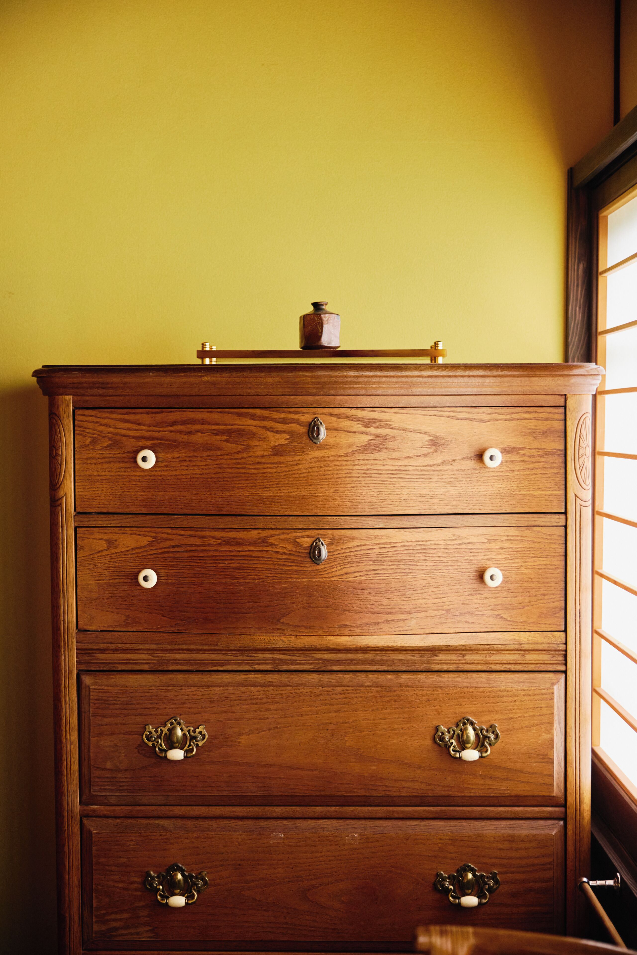Une commode en bois, dotée de tiroirs et de poignées, est placée contre un mur jaune.