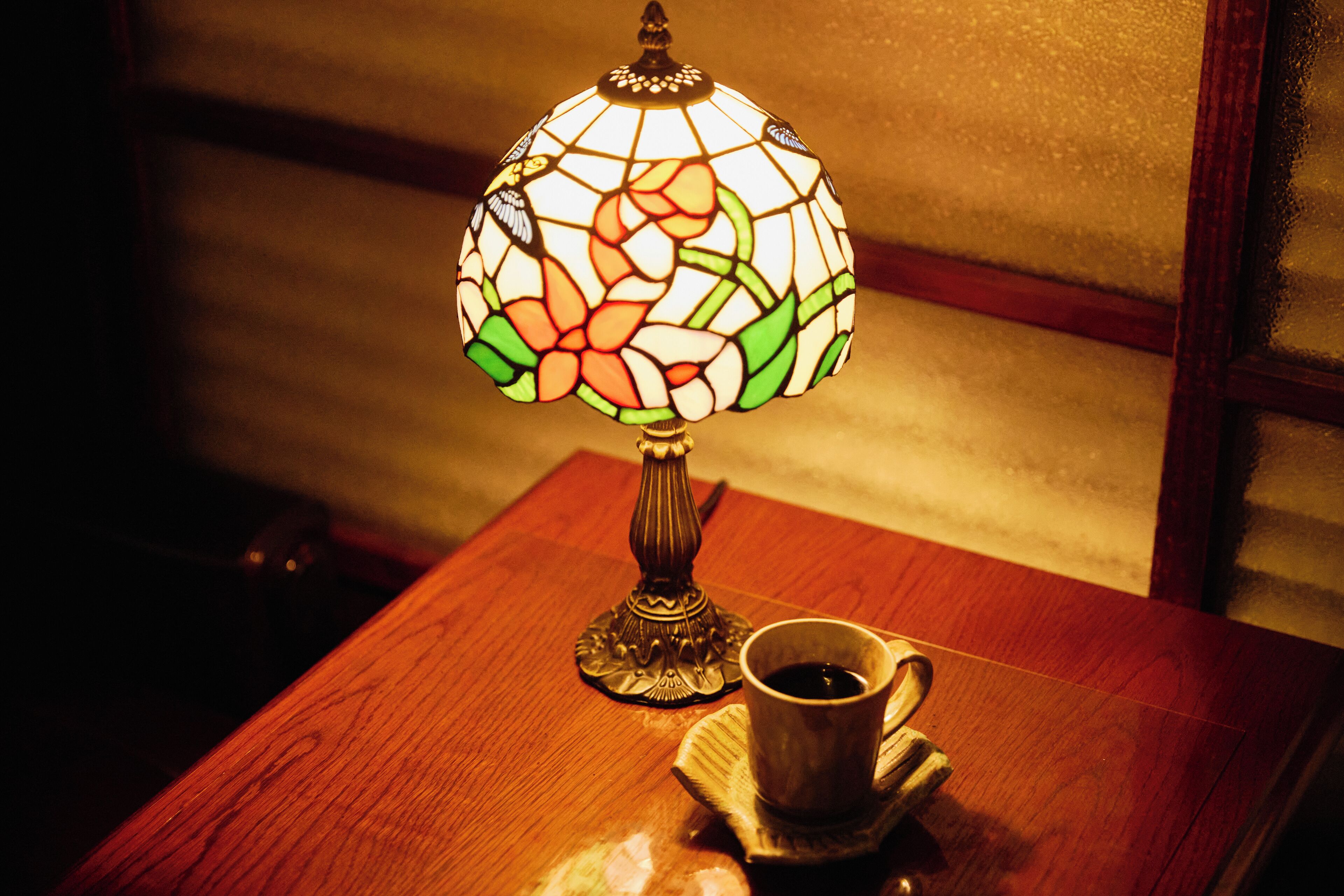 A table with a stained glass lamp and a cup of coffee.