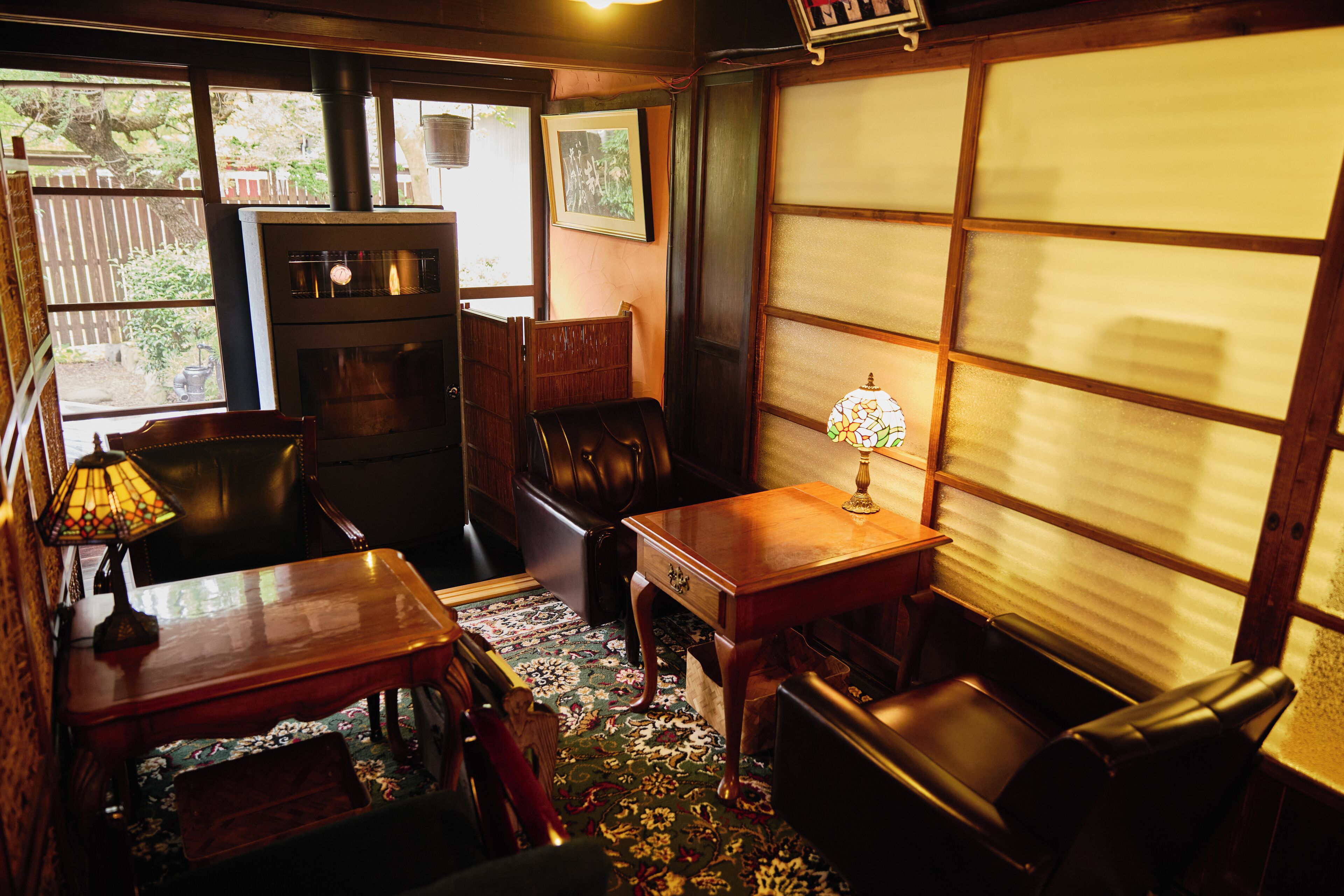 A traditional room with a wooden table, chairs, a lamp, and a view through a shoji screen.