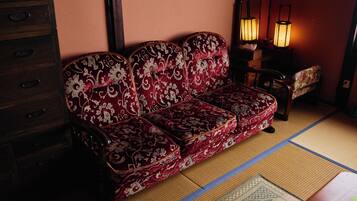 A traditional Japanese room with tatami flooring, a red patterned sofa, a wooden cabinet, and two floor lamps.