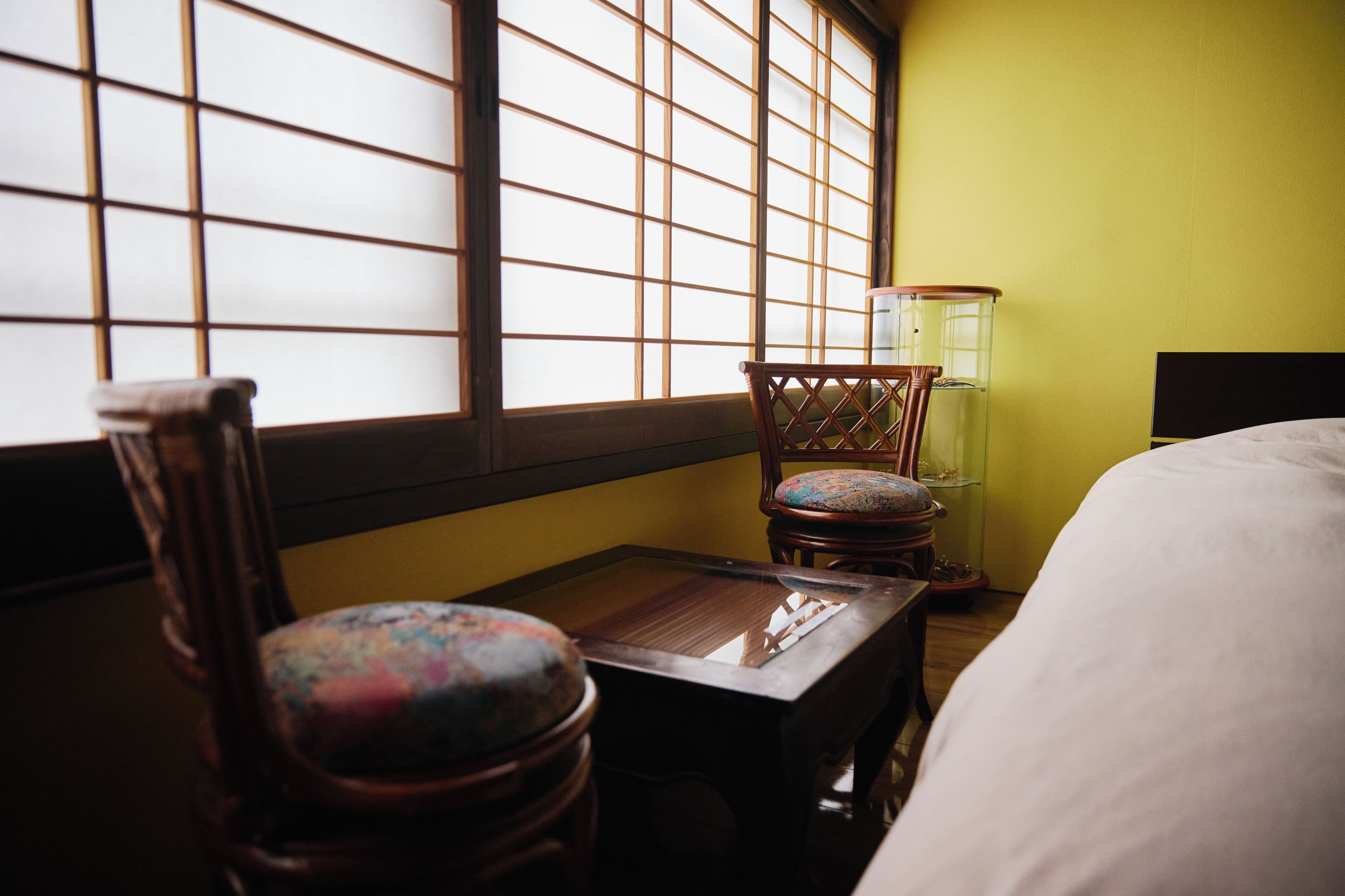 A room with a bed, a wooden table, a chair, and a lamp.