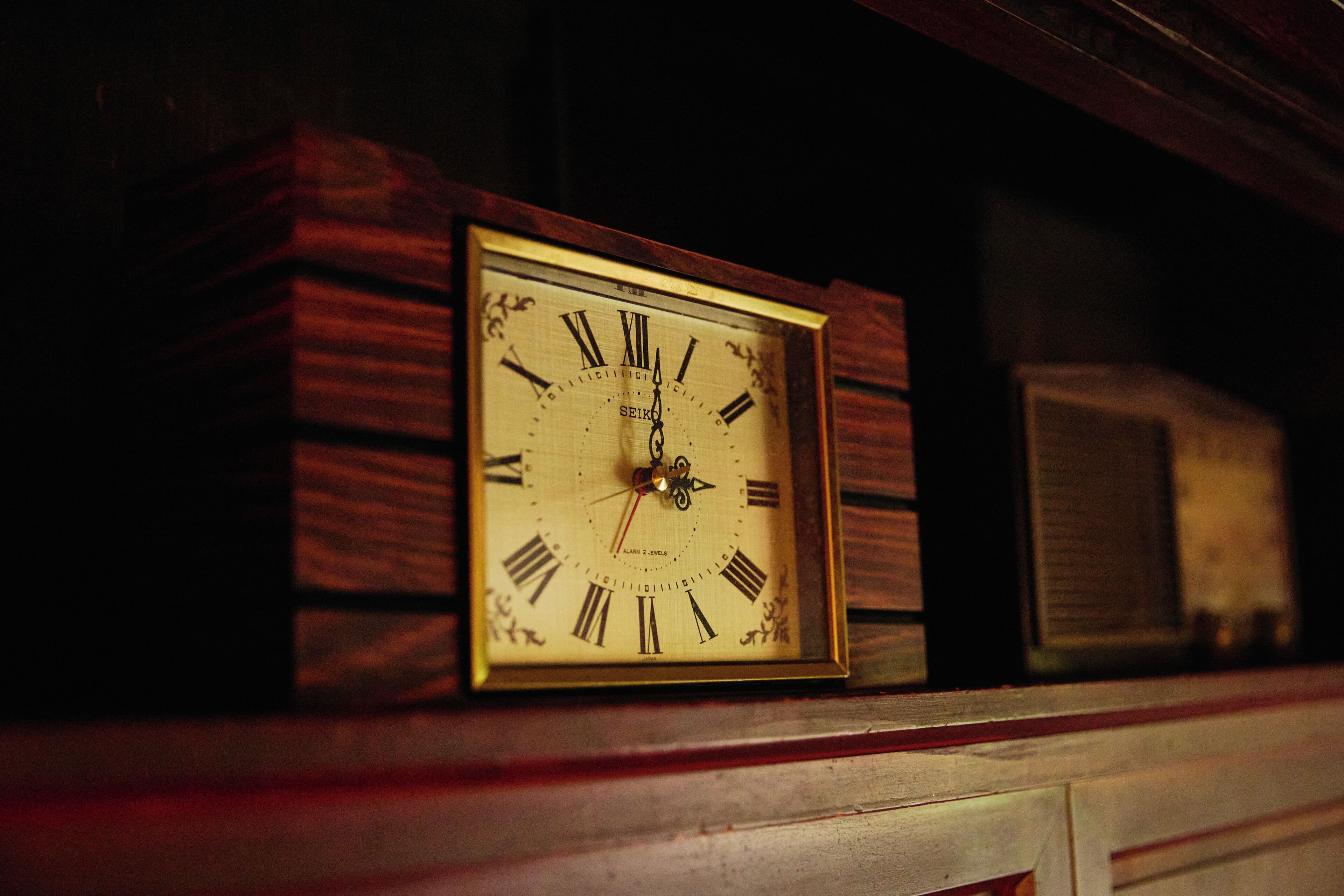 Un reloj de pared con números romanos y péndulo, enmarcado en madera.