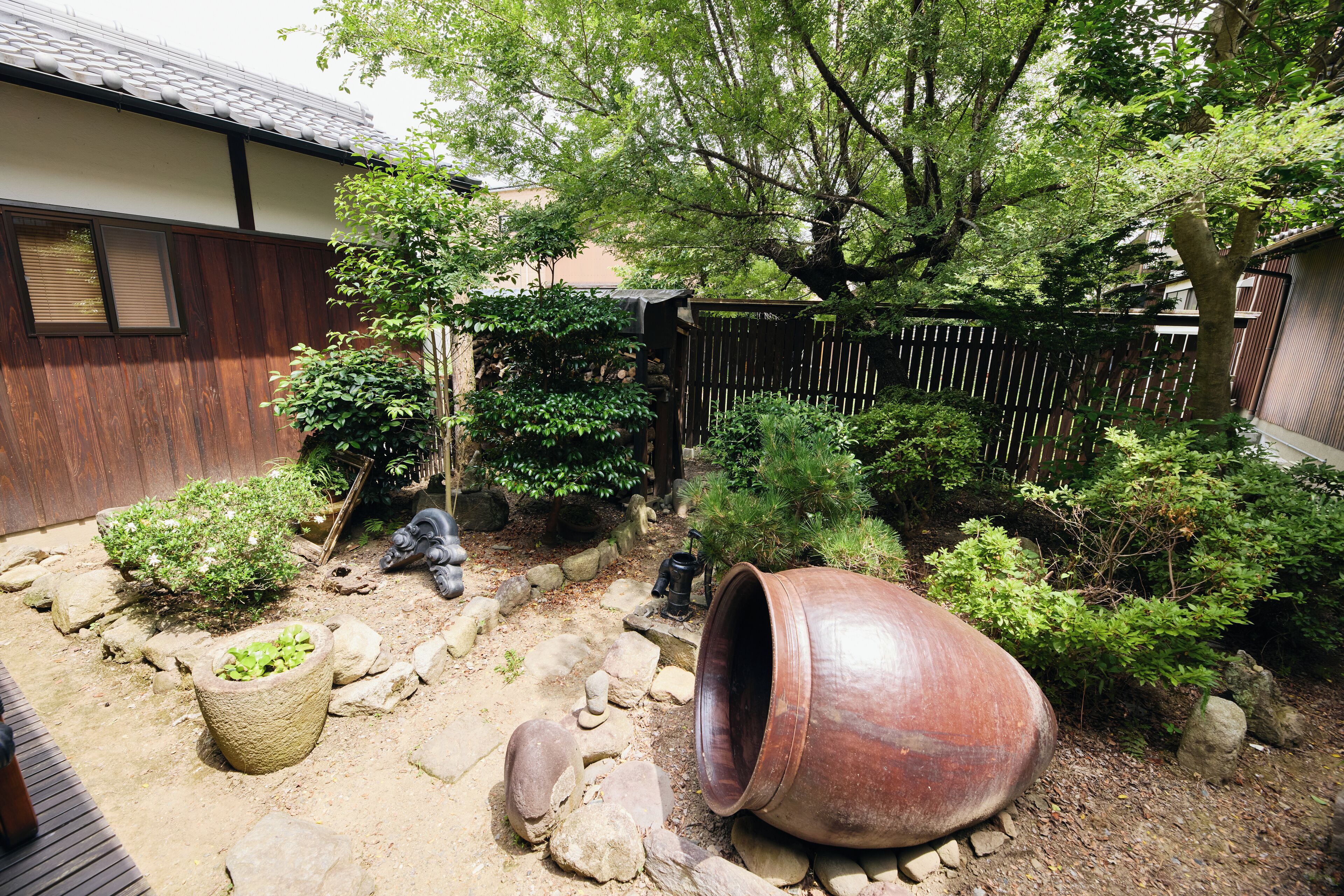 A garden with a large pot, rocks, and various plants.