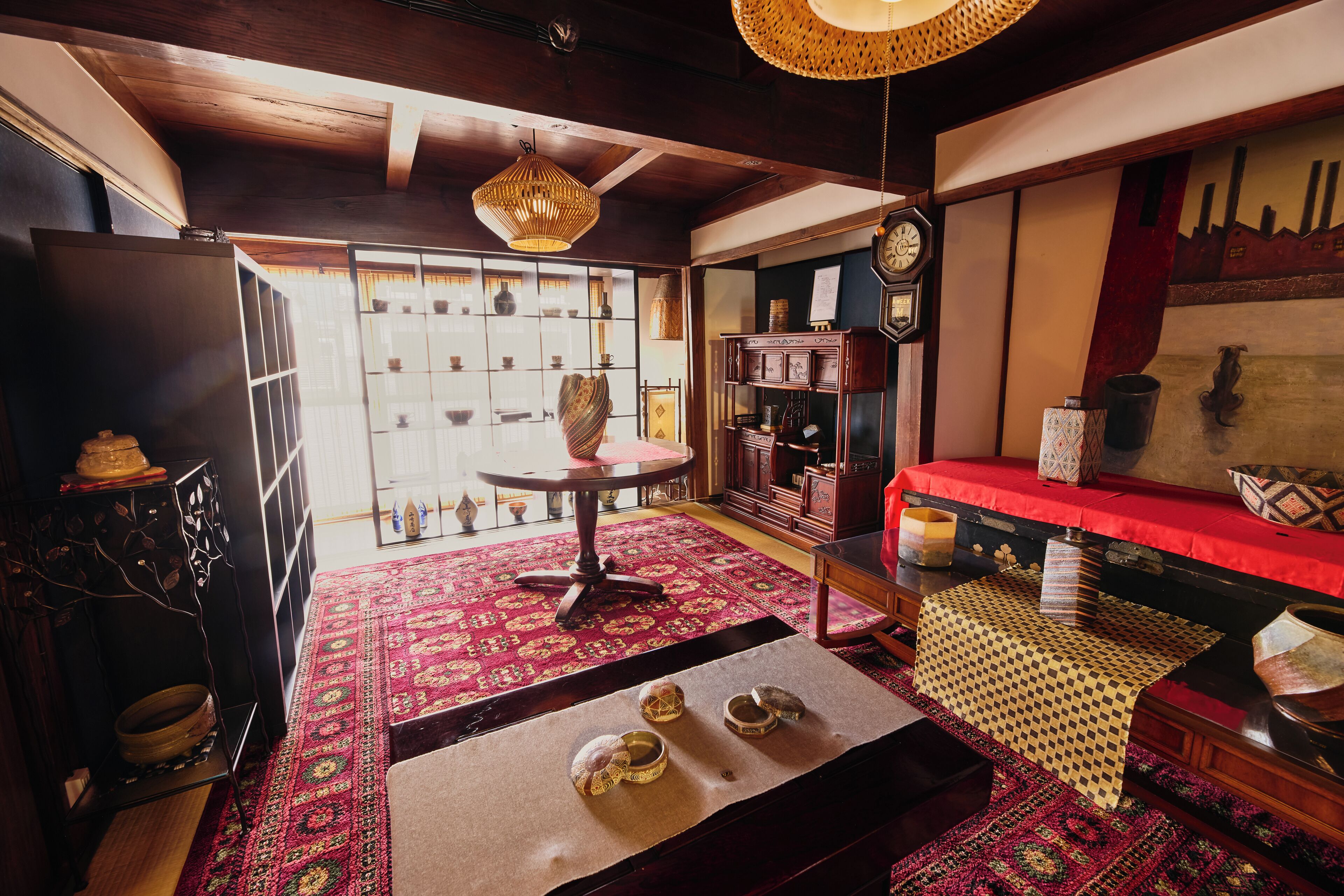 A traditional room with a wooden ceiling, a red sofa, a patterned rug, and a table with bowls.