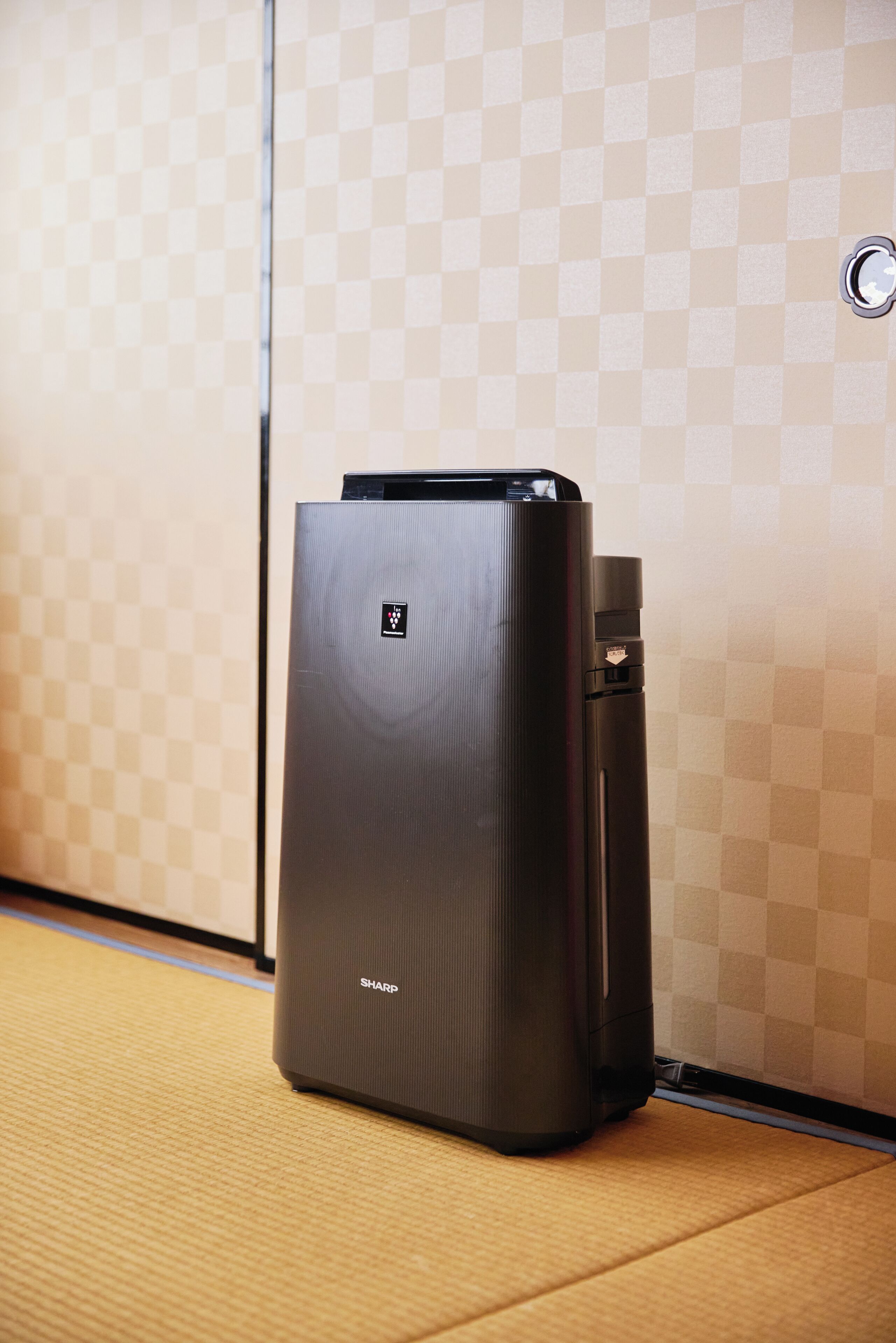 Un refrigerador Sharp negro en una habitación con un estampado de cuadros.