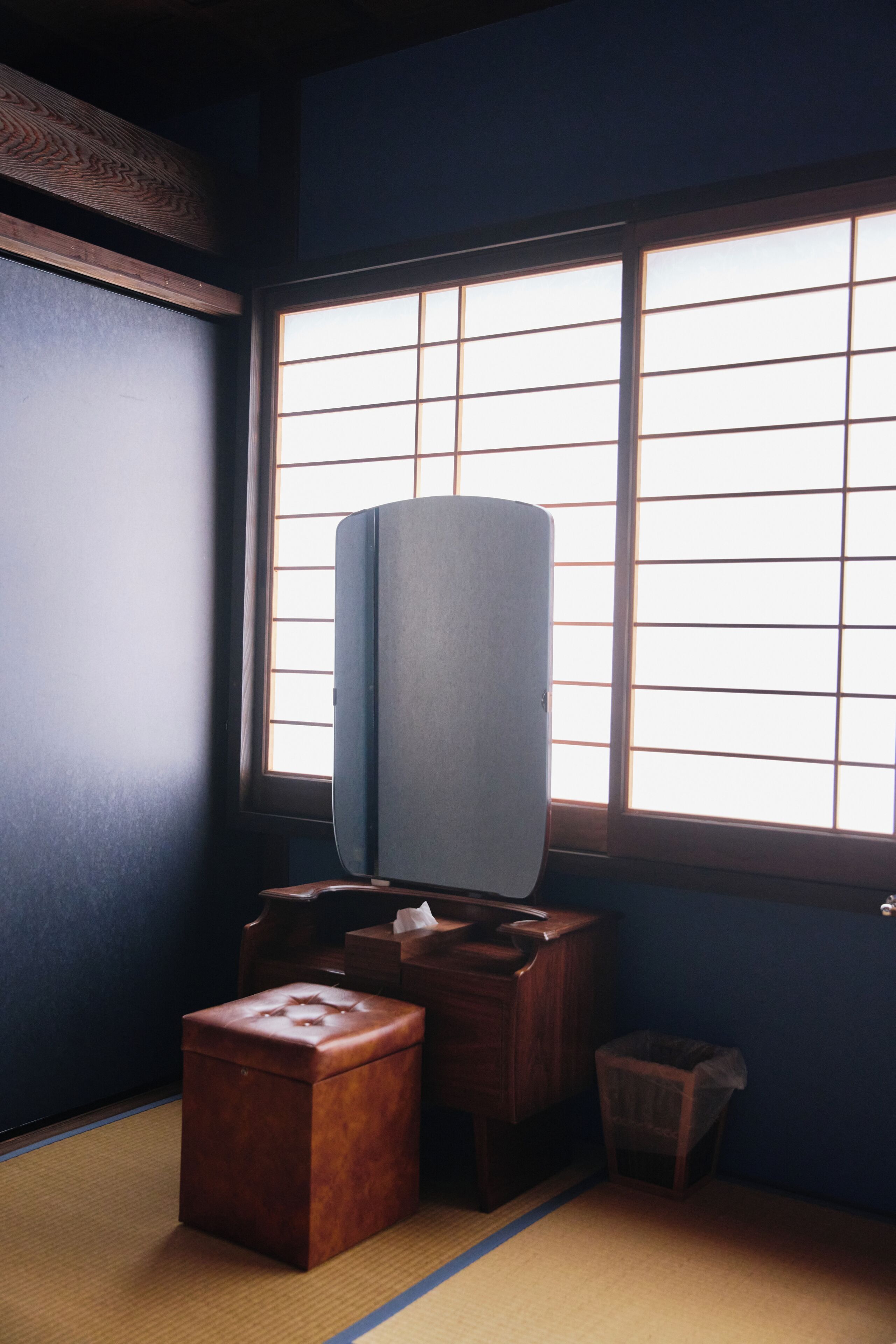 A traditional Japanese room with tatami flooring, a wooden desk, a television, and a window with a grid pattern.