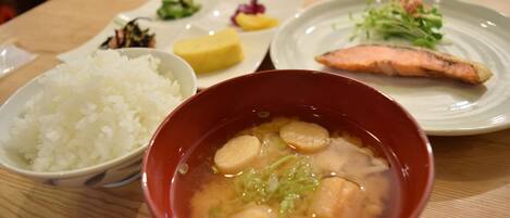 Una mesa con un tazón de arroz, un tazón de sopa, un plato con un trozo de salmón y un plato con una pequeña guarnición de vegetales encurtidos.
