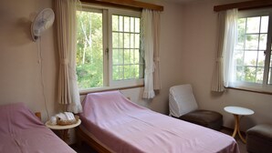 A room with two beds, a chair, a small table, and a fan.