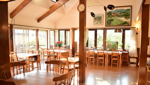 A spacious dining area with wooden tables and chairs, large windows with curtains, and a clock on the wall.