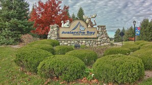 Een bord voor Avalanche Bay Indoor Waterpark, met een moose en een hondenbeeld, omringd door keurig gesnoeide struiken.