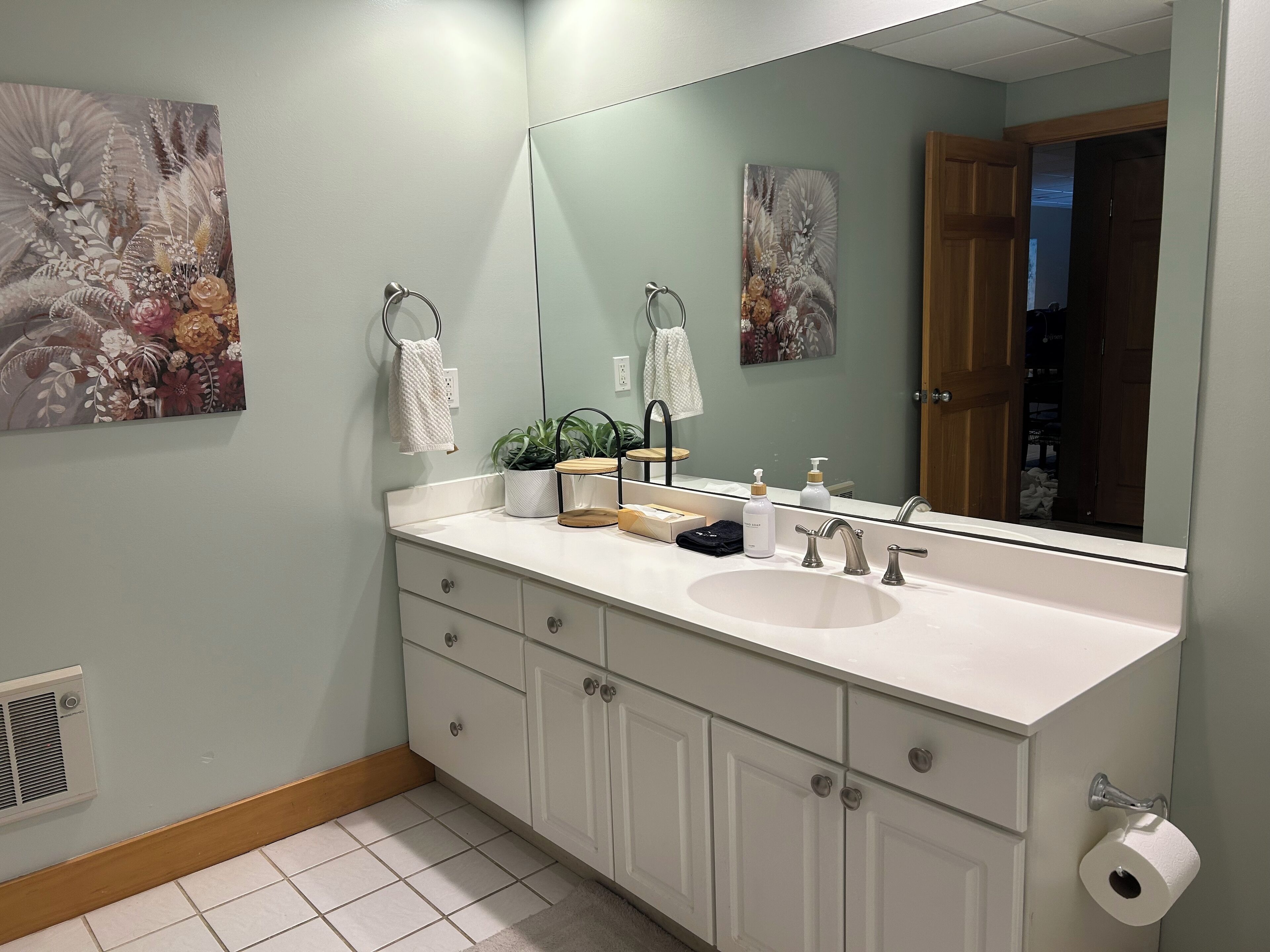 Un bagno con un mobile lavabo bianco, un ampio specchio e due porta asciugamani a parete.