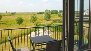 A balcony with a table and chairs, overlooking a grassy field and trees. - Ganuenta by Interhome (Colijnsplaat)