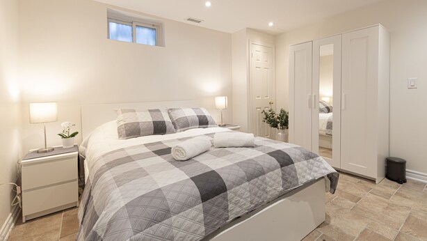 A neatly arranged bedroom with a bed, bedside tables, a wardrobe, and a small window.