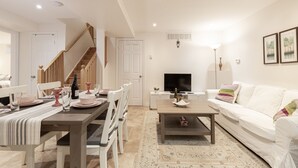 A modern living room with a dining area, a staircase, a flat-screen TV, and a white couch.