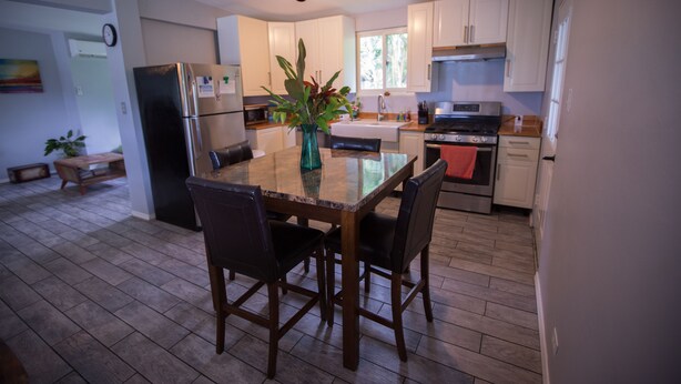 A modern kitchen with white cabinets, a stainless steel refrigerator, a dining table with chairs, and a potted plant.