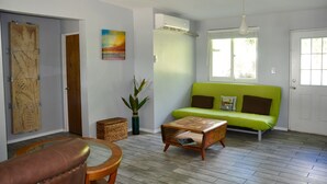 A living room with a green sofa, a wooden coffee table, a brown leather chair, a map on the wall, and a window with a view.