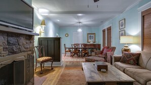 A living room with a fireplace, a dining table with chairs, a sofa, and a television mounted on the wall. - 3BR 2BA Dynamite Cooper Young Craftsman 2 blocks from Cooper Young intersection! (Memphis)