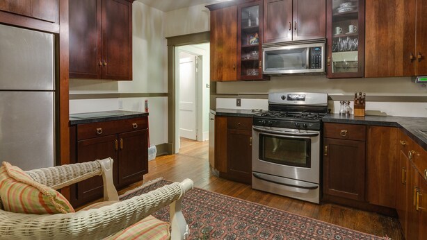 A kitchen with wooden cabinets, a microwave, stove, and a wicker chair. - 3BR 2BA Dynamite Cooper Young Craftsman 2 blocks from Cooper Young intersection! (Memphis)