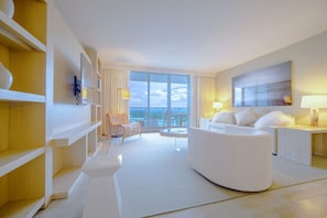 Una habitación de hotel moderna con un sofá blanco, una silla de mimbre y un ventanal con vistas al cielo y las nubes.