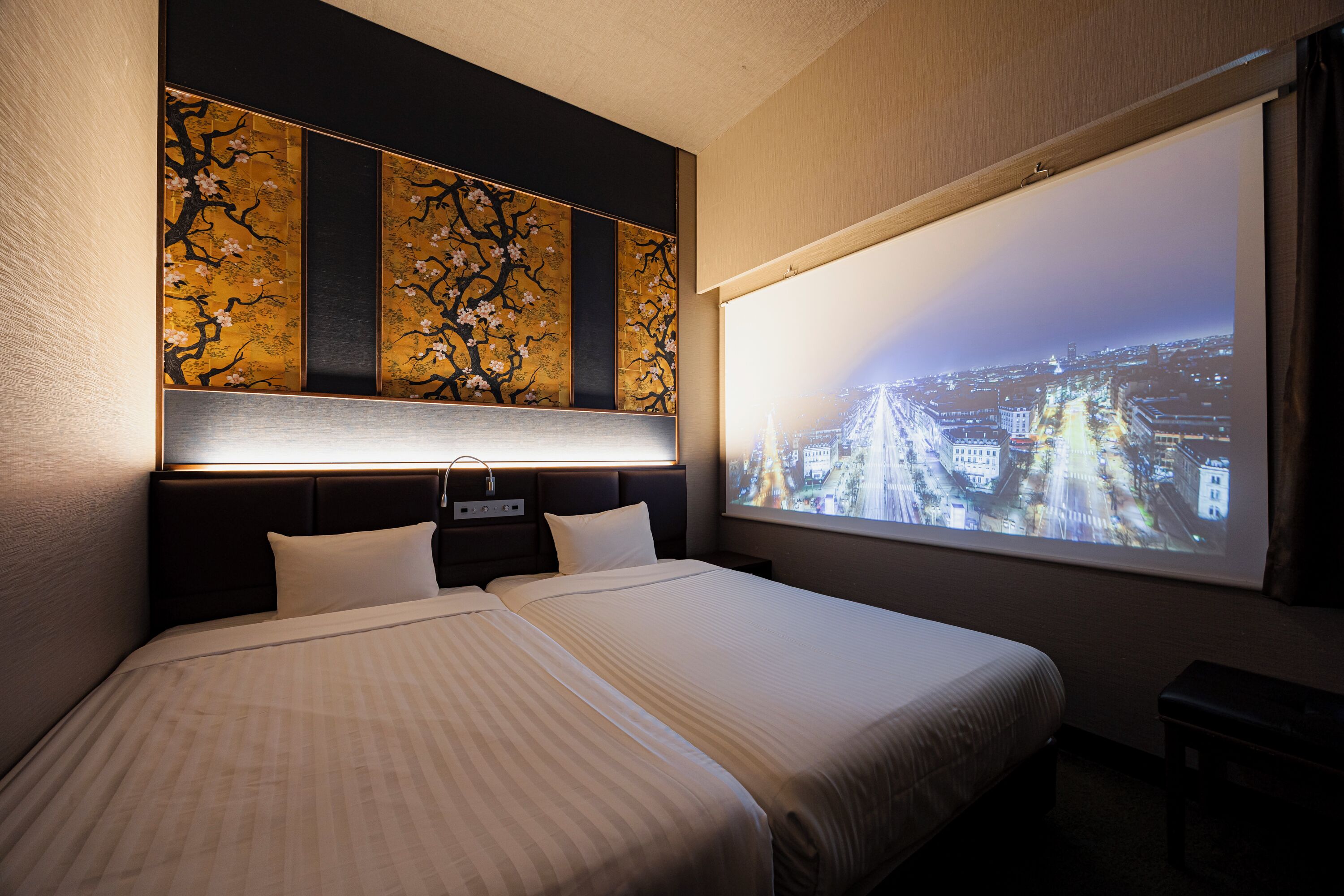 A hotel room with a bed, a nightstand, a wall-mounted TV, and a view of a cityscape.