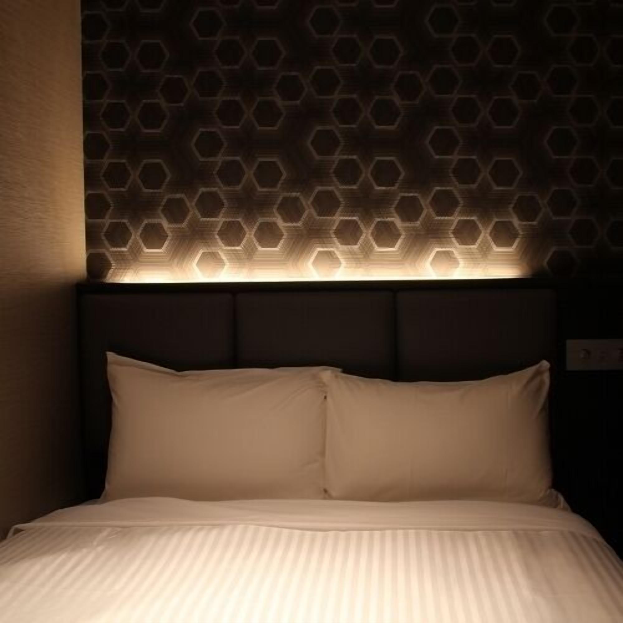 Ein Bett mit Kopfteil, das ein geometrisches Muster zeigt, und einer Lichtquelle darunter.