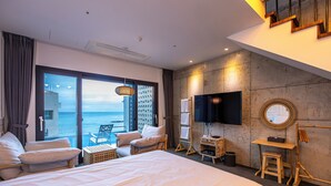 Habitació d'hotel amb un llit gran, una taula de treball, una cadira i un televisor. Hi ha un balcó amb vista al mar.