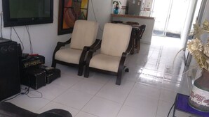 A living room with two beige armchairs, a TV, a sound system, and a dining area with a table and chairs.