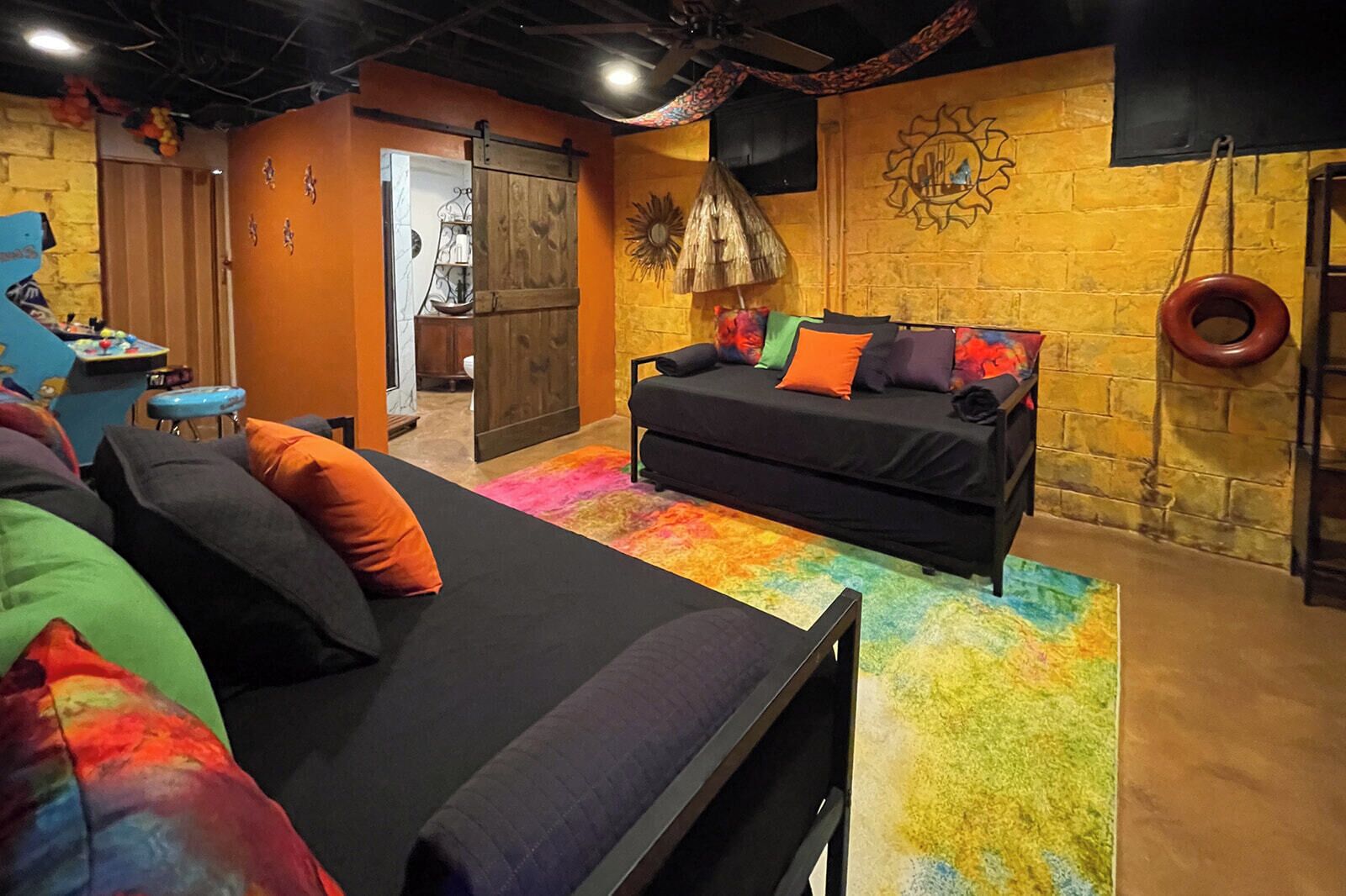 A cozy room with a black sofa, colorful pillows, a small table, and a vibrant rug.