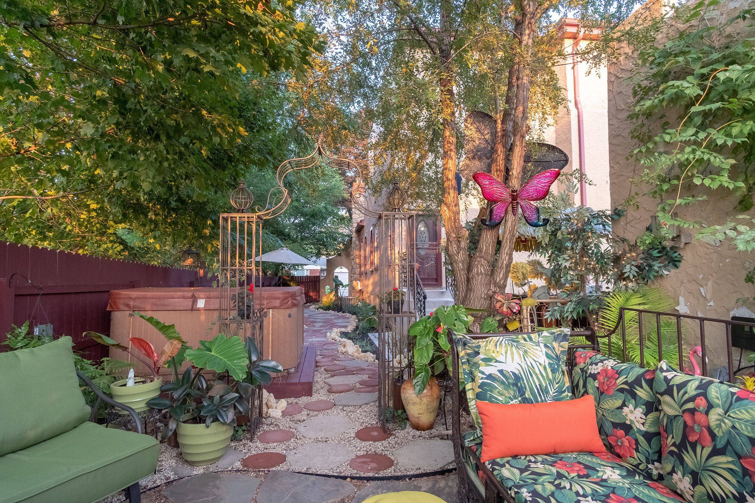 A garden patio with a pathway, seating areas, and decorative elements like a butterfly sculpture and a tree.