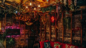 A cozy room with a red sofa, wicker furniture, and a variety of plants and decorations.