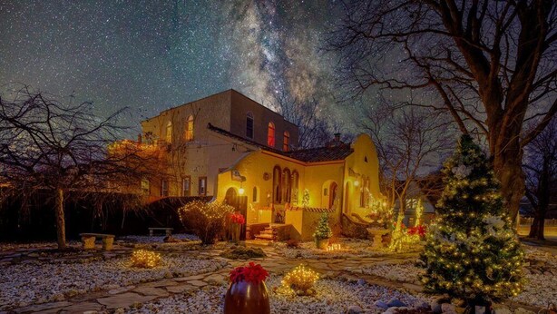 A house with a stone pathway leading to the entrance, surrounded by trees and decorated with lights and a Christmas tree.