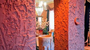 An interior view through a textured archway with a chandelier, a mirror, and a vase of flowers.