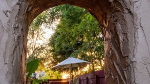 Un arco de entrada que da a un patio con un camino de piedra, mobiliario exterior y una valla de madera.