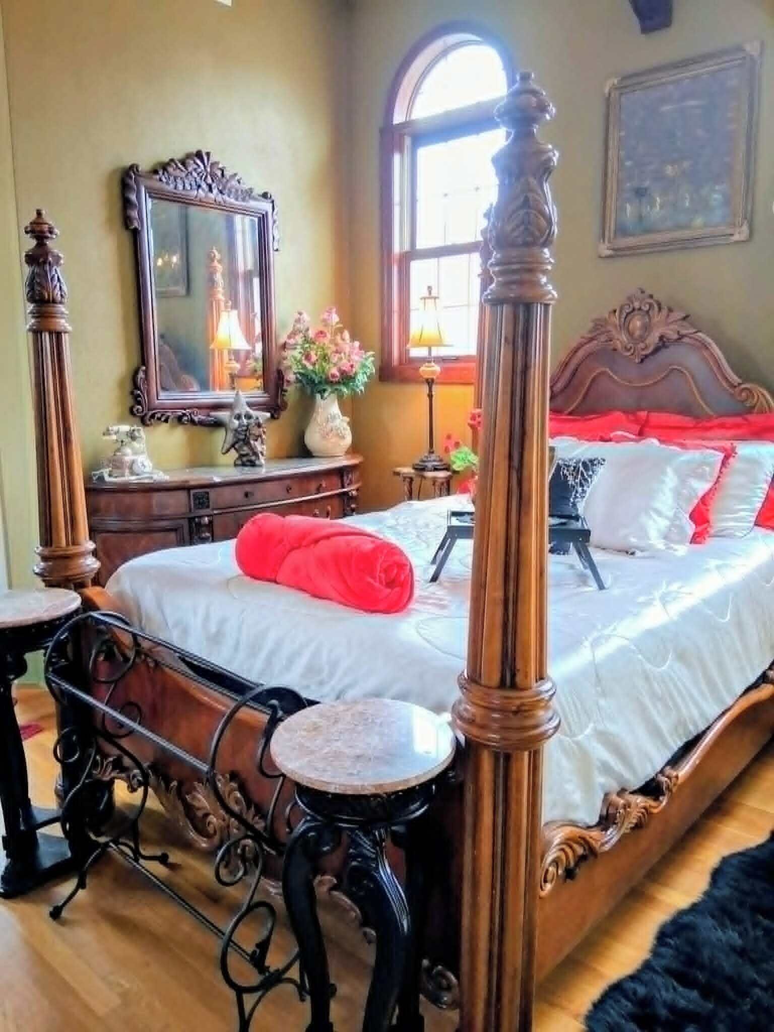 A bedroom with a four-poster bed, a dresser, a mirror, and a window with natural light.