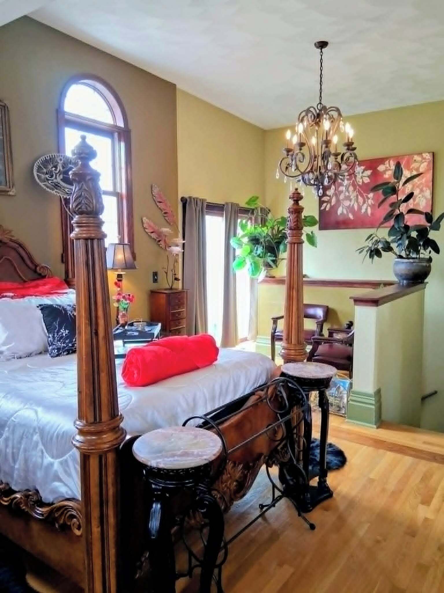 A bedroom with a large bed, a chandelier, and a view of the living area.