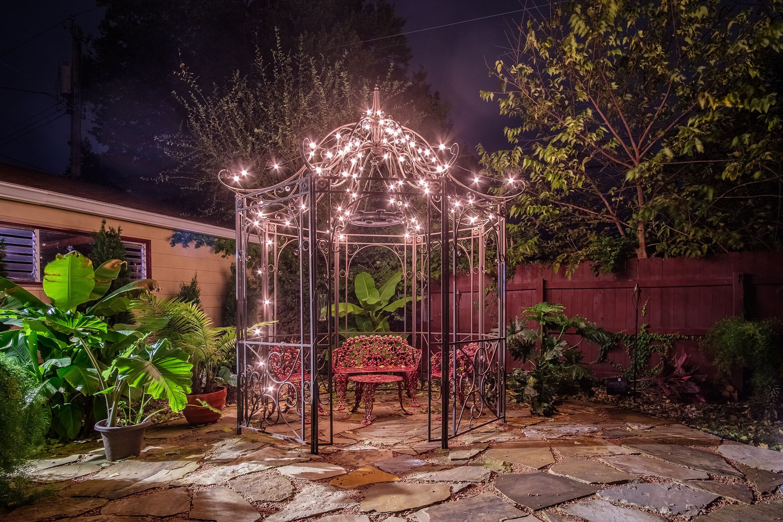A gazebo with a bench, surrounded by potted plants and a stone pathway.