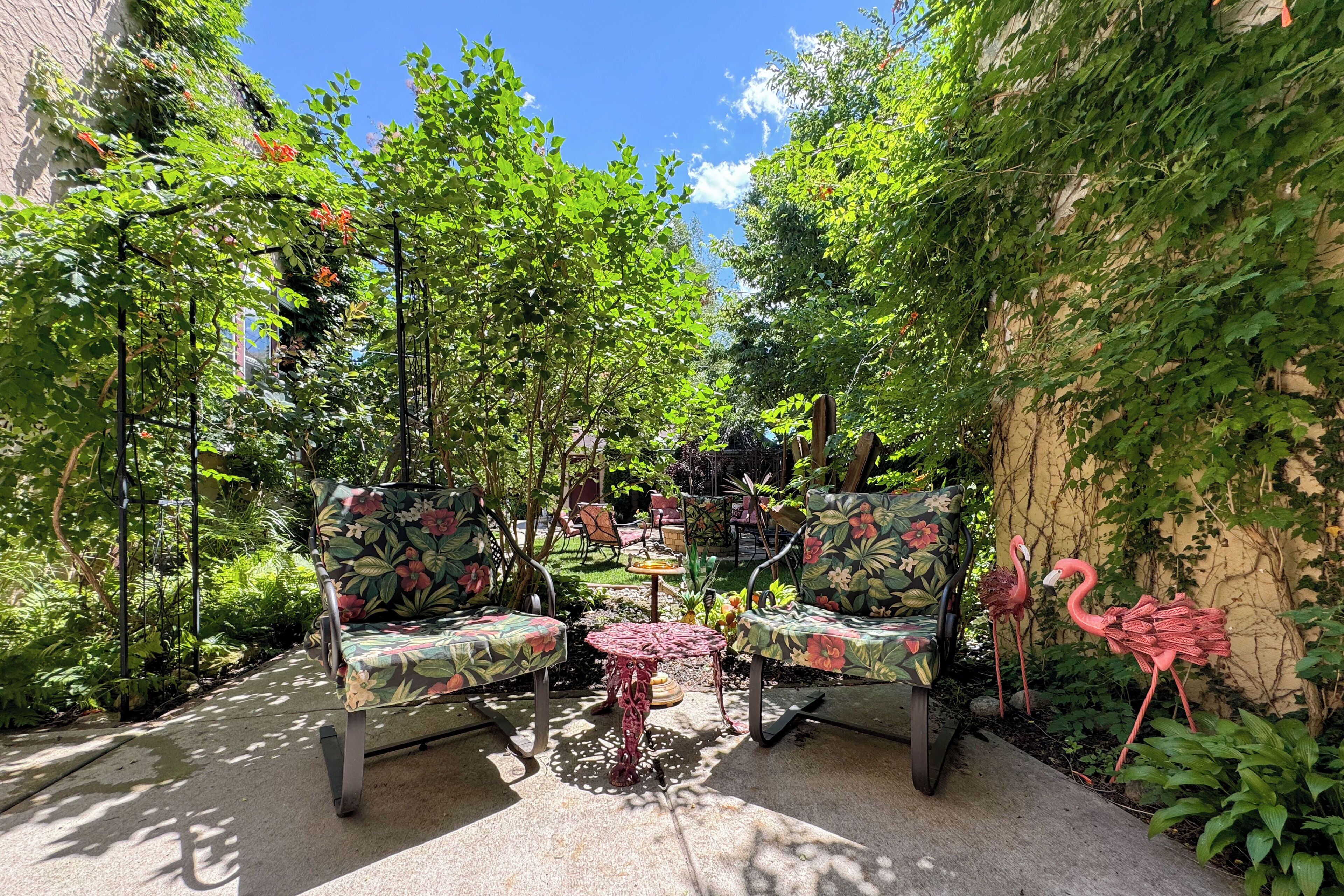 Un espace extérieur aménagé avec des chaises et une table, entouré de verdure et d’un mur recouvert de plantes grimpantes.
