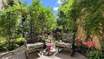 Un espace extérieur aménagé avec des chaises et une table, entouré de verdure et d’un mur recouvert de plantes grimpantes.