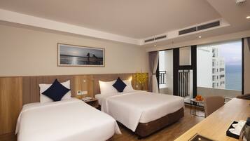 A hotel room with two beds, a dining table, a small table with fruit, and a view of the sea.