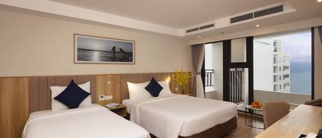 A hotel room with two beds, a dining table, a small table with fruit, and a view of the sea.