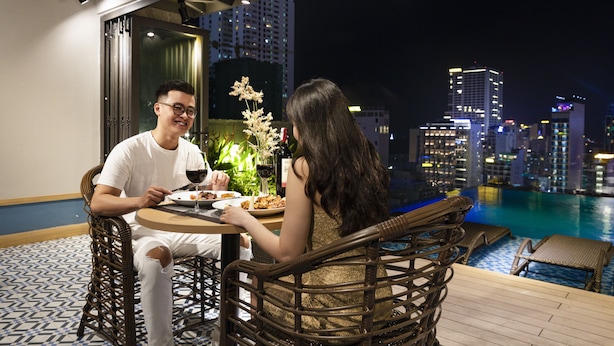 A couple dining at a table with a city view, near a pool.