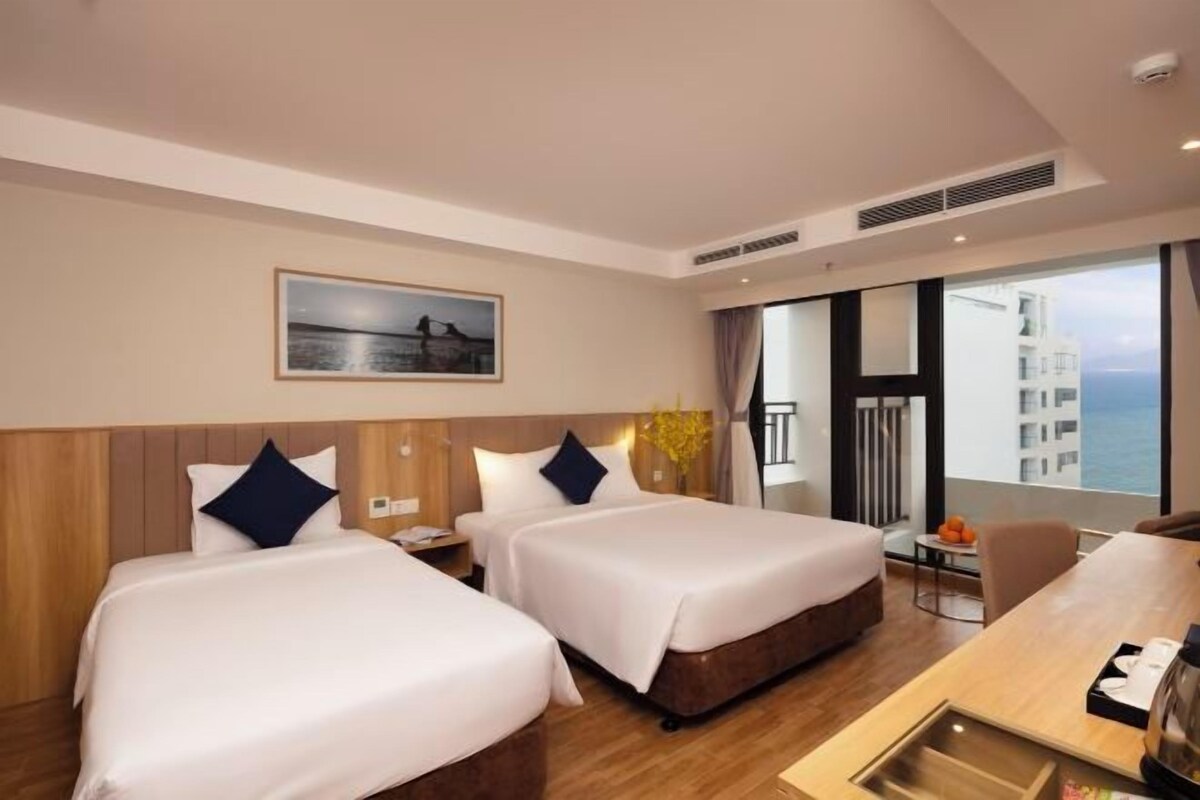 Une chambre d’hôtel avec deux lits, un bureau et vue sur la mer.