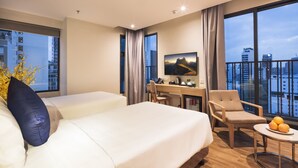 A hotel room with two beds, a desk, a chair, a TV, and a balcony with a city view.