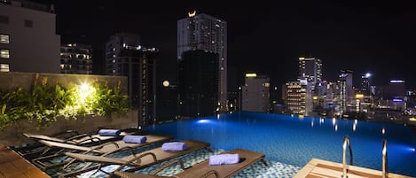 Piscina en la azotea con sillones de descanso y vista panorámica al horizonte urbano de noche.