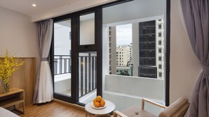 Une chambre d’hôtel moderne avec un balcon, une petite table ronde ornée d’oranges et une vue sur le paysage urbain.