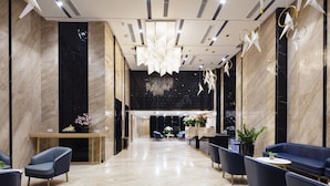 A modern lobby with a marble floor, blue seating, a reception desk, and a chandelier.