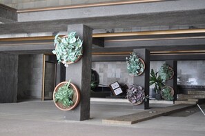 A lobby with multiple planters, a reception desk, and a stone wall. - Hotel Flamingo Kristal (Irapuato)