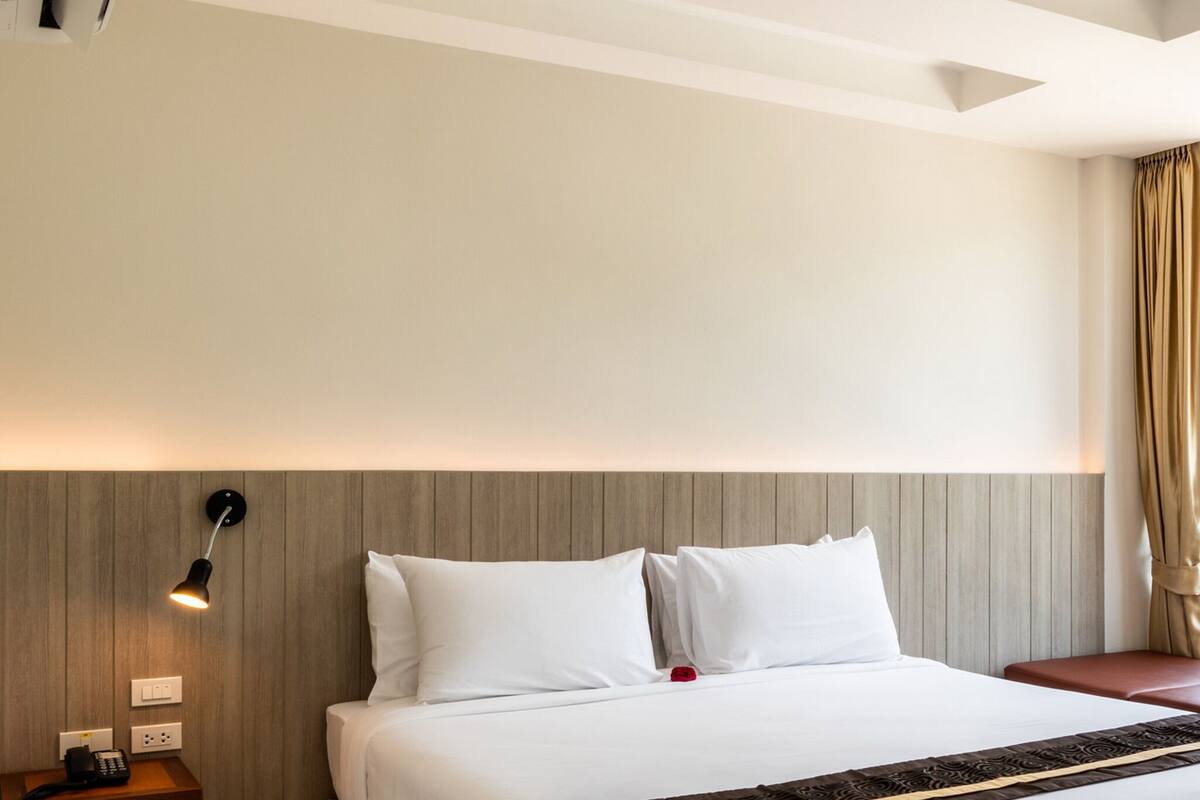 Ein Hotelzimmer mit Bett, Nachttisch, Lampe und Wandgerät zur Klimatisierung.