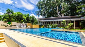 A hotel pool area with a clear view of the pool, lounge chairs, and a building with a sign. - Ozone Hotel Khao Yai (Pak Chong)